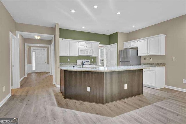 kitchen featuring stainless steel refrigerator, white cabinetry, a center island with sink, light stone counters, and light wood-type flooring