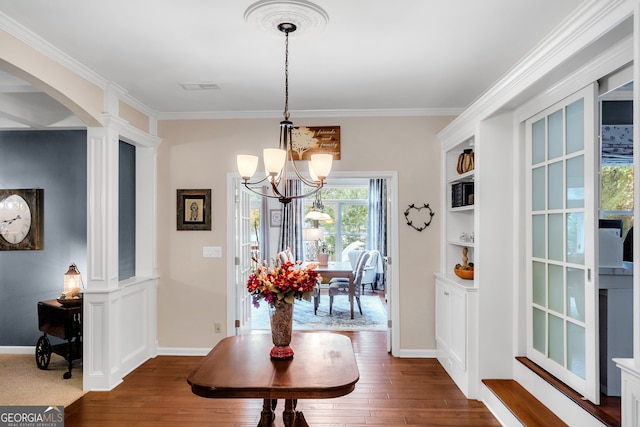 dining area featuring ornamental molding, an inviting chandelier, dark wood-type flooring, built in features, and ornate columns