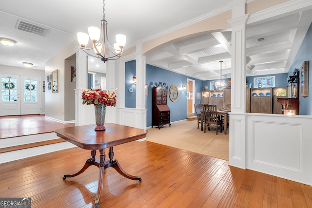 foyer entrance with ornate columns, a chandelier, coffered ceiling, beam ceiling, and light hardwood / wood-style flooring