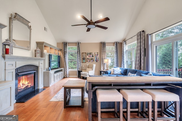 living room with a premium fireplace, ceiling fan, high vaulted ceiling, and light hardwood / wood-style floors