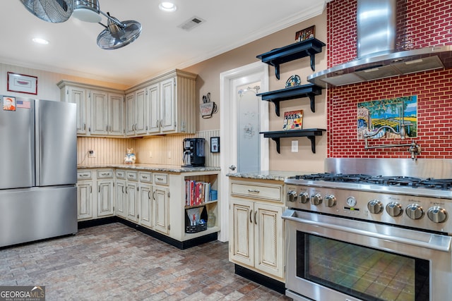 kitchen with cream cabinetry, wall chimney exhaust hood, appliances with stainless steel finishes, and tasteful backsplash