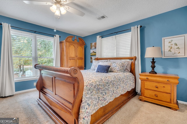 bedroom featuring ceiling fan, multiple windows, a textured ceiling, and light colored carpet