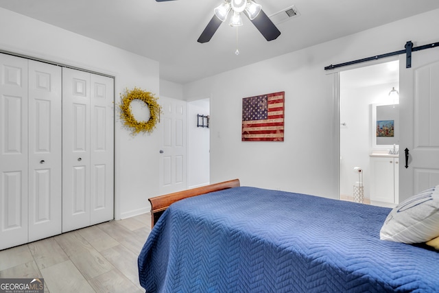 bedroom featuring light hardwood / wood-style flooring, a barn door, ceiling fan, and a closet