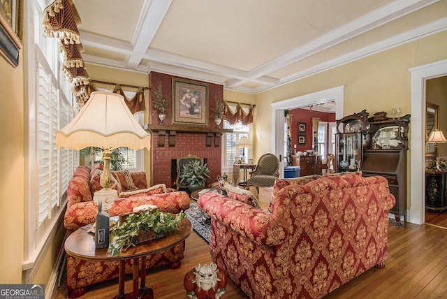 living area featuring coffered ceiling, hardwood / wood-style floors, crown molding, a brick fireplace, and beam ceiling