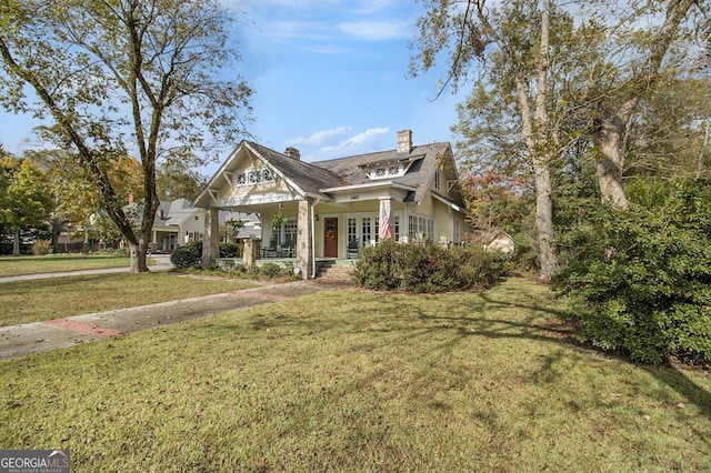 view of front of property with covered porch, a chimney, and a front yard