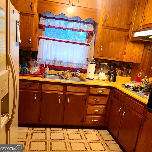 kitchen featuring a sink, light countertops, freestanding refrigerator, backsplash, and stainless steel gas cooktop