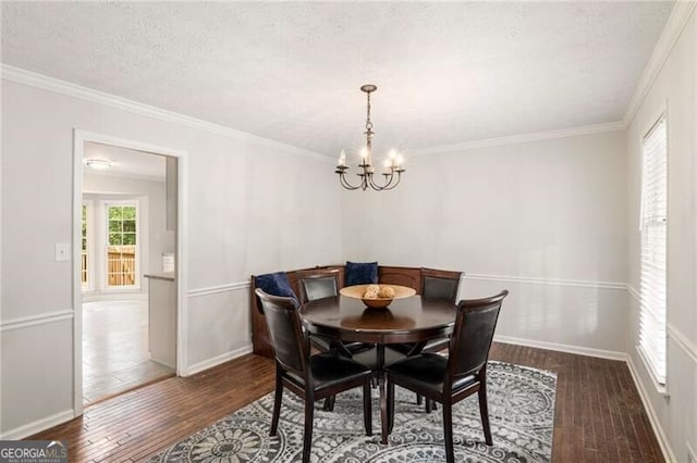 dining room with dark wood-type flooring, a chandelier, a textured ceiling, and ornamental molding