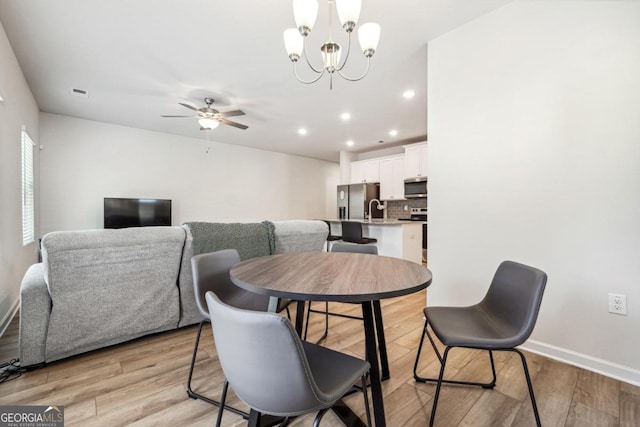 dining space featuring light hardwood / wood-style floors, ceiling fan with notable chandelier, and sink