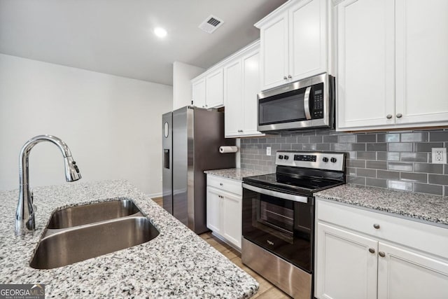 kitchen featuring light hardwood / wood-style floors, white cabinetry, sink, light stone counters, and appliances with stainless steel finishes