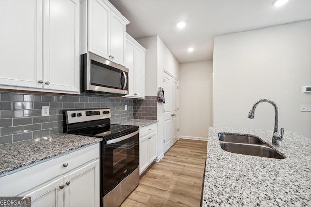 kitchen with light hardwood / wood-style floors, light stone counters, sink, white cabinetry, and appliances with stainless steel finishes