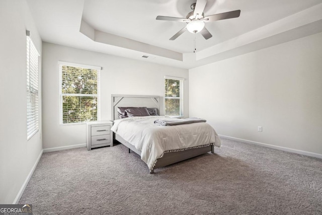 bedroom with light carpet, ceiling fan, and a raised ceiling