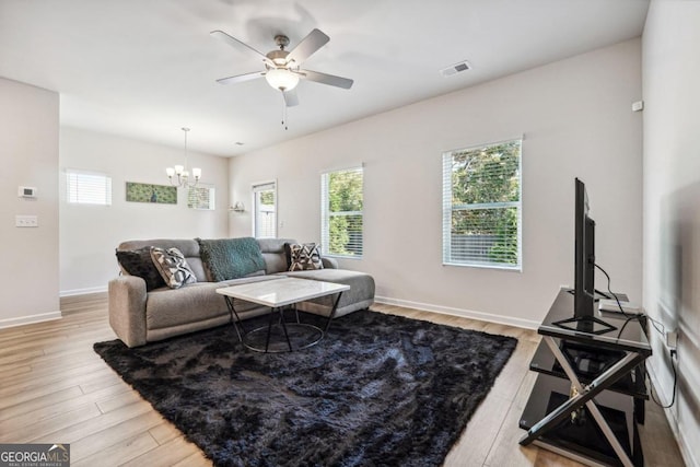 living room with ceiling fan with notable chandelier and light hardwood / wood-style flooring