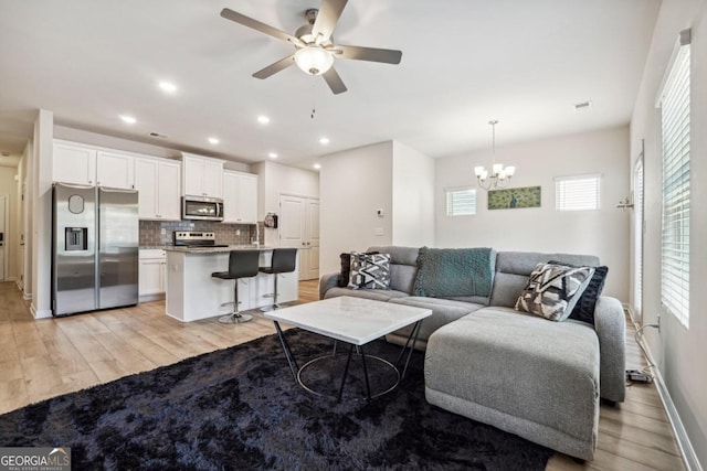 living room with a wealth of natural light, ceiling fan with notable chandelier, and light hardwood / wood-style floors