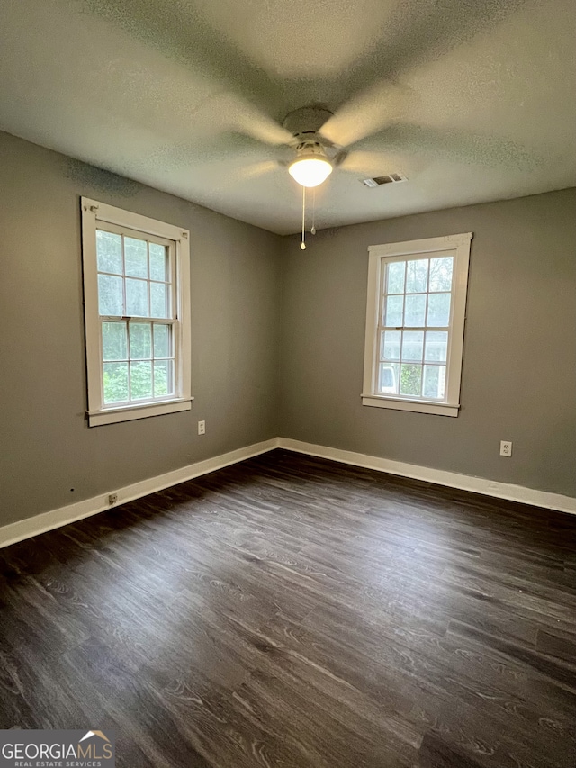 unfurnished room with ceiling fan, a healthy amount of sunlight, dark wood-type flooring, and a textured ceiling