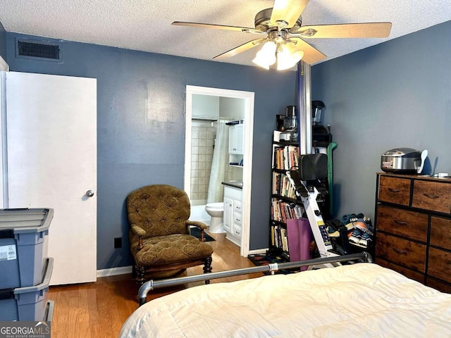 bedroom featuring ceiling fan, ensuite bath, a textured ceiling, and dark hardwood / wood-style flooring