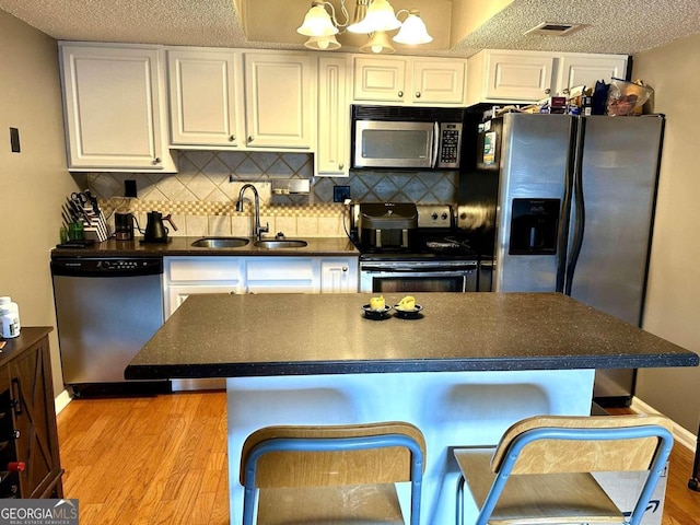 kitchen featuring stainless steel appliances, light hardwood / wood-style floors, white cabinetry, sink, and a breakfast bar area