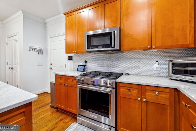 kitchen featuring light stone countertops, appliances with stainless steel finishes, crown molding, and light hardwood / wood-style flooring