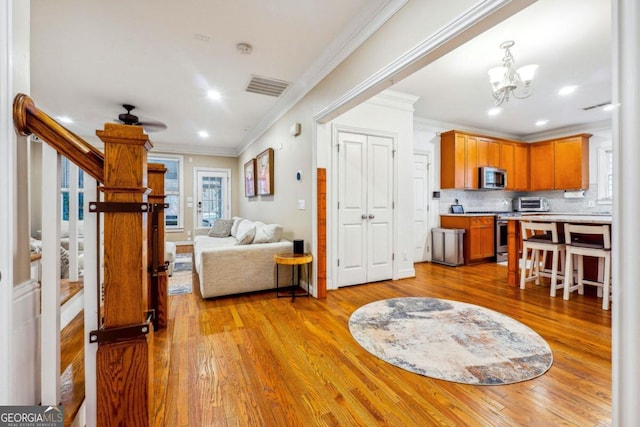 kitchen featuring crown molding, backsplash, appliances with stainless steel finishes, light hardwood / wood-style floors, and ceiling fan with notable chandelier