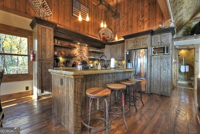 bar with high vaulted ceiling, appliances with stainless steel finishes, wood walls, and dark hardwood / wood-style flooring