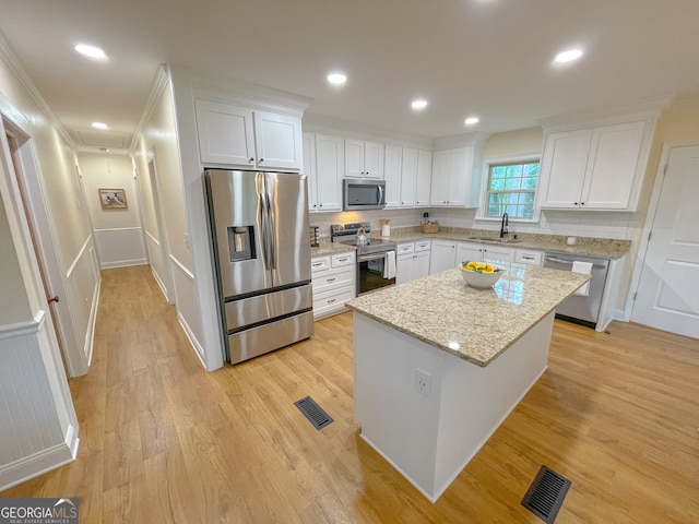 kitchen with light hardwood / wood-style floors, a center island, white cabinets, light stone countertops, and appliances with stainless steel finishes