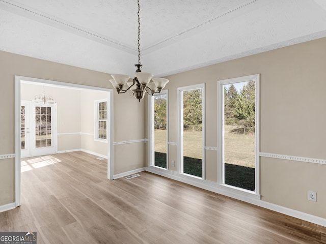 unfurnished dining area featuring hardwood / wood-style floors, a textured ceiling, and a notable chandelier