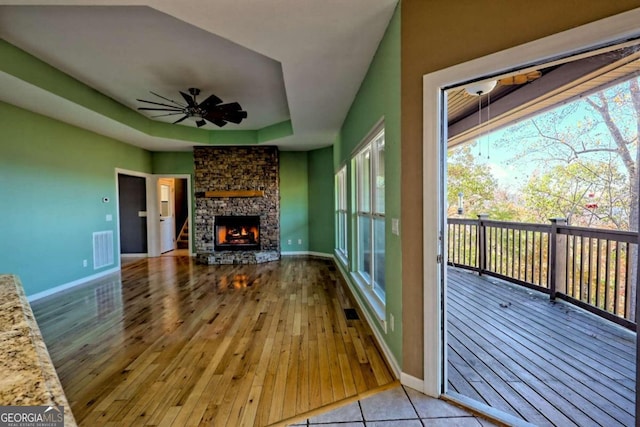 unfurnished living room with ceiling fan, a stone fireplace, and light wood-type flooring