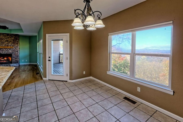 unfurnished dining area with a fireplace, a wealth of natural light, light hardwood / wood-style flooring, and a notable chandelier