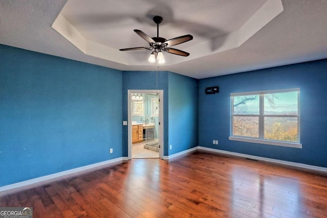 unfurnished bedroom featuring a tray ceiling, wood-type flooring, ceiling fan, and ensuite bathroom