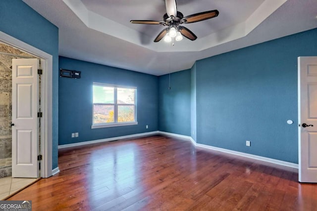 empty room featuring hardwood / wood-style floors, ceiling fan, and a raised ceiling