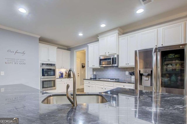 kitchen featuring white cabinets, sink, ornamental molding, appliances with stainless steel finishes, and dark stone countertops