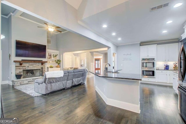 kitchen featuring a stone fireplace, white cabinets, stainless steel double oven, dark hardwood / wood-style floors, and dark stone countertops