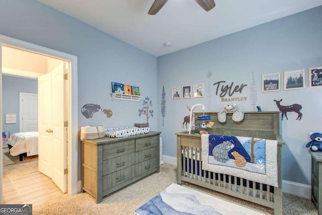 bedroom with a crib, light hardwood / wood-style floors, and ceiling fan