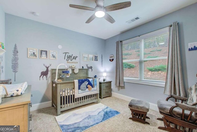 carpeted bedroom featuring a nursery area and ceiling fan