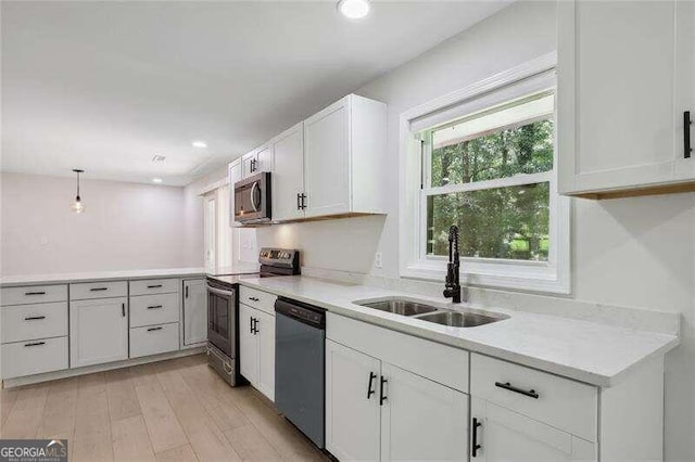 kitchen featuring stainless steel appliances, white cabinetry, sink, hanging light fixtures, and light hardwood / wood-style flooring