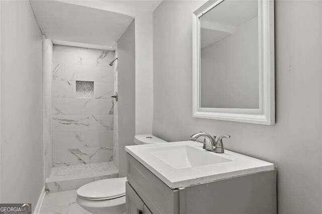 bathroom featuring toilet, vanity, and a tile shower