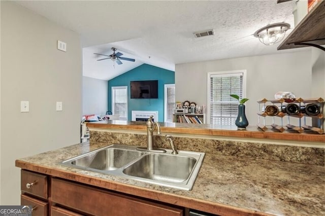 kitchen with sink, ceiling fan, a textured ceiling, a large fireplace, and vaulted ceiling