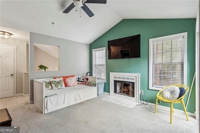 bedroom featuring a tiled fireplace, light carpet, ceiling fan, and vaulted ceiling