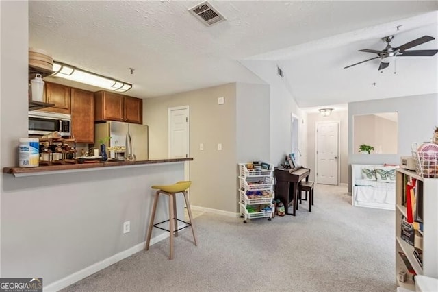 kitchen featuring stainless steel appliances, a kitchen breakfast bar, kitchen peninsula, light colored carpet, and ceiling fan