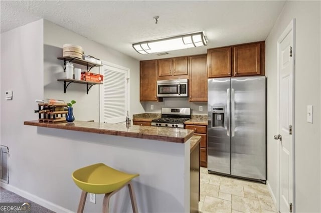 kitchen with stainless steel appliances, a textured ceiling, a breakfast bar area, dark stone countertops, and kitchen peninsula