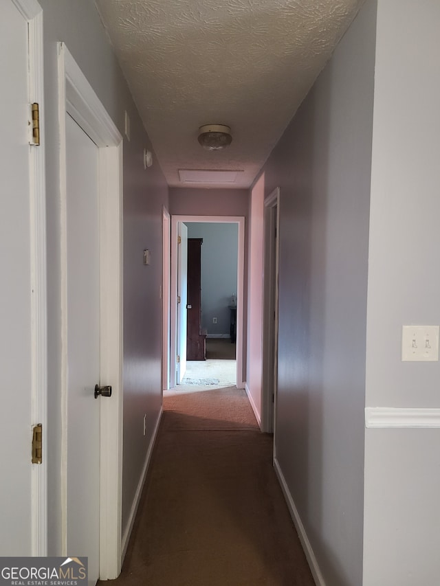 corridor with a textured ceiling and dark carpet