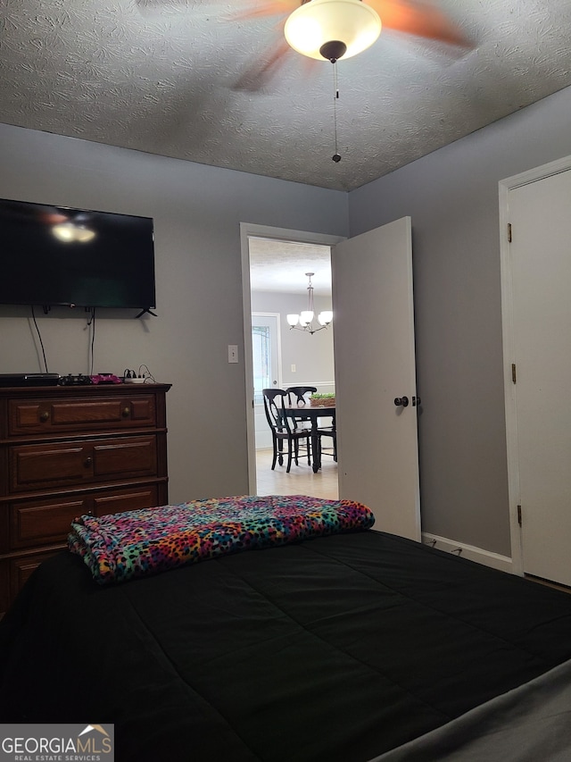 bedroom featuring ceiling fan with notable chandelier and a textured ceiling