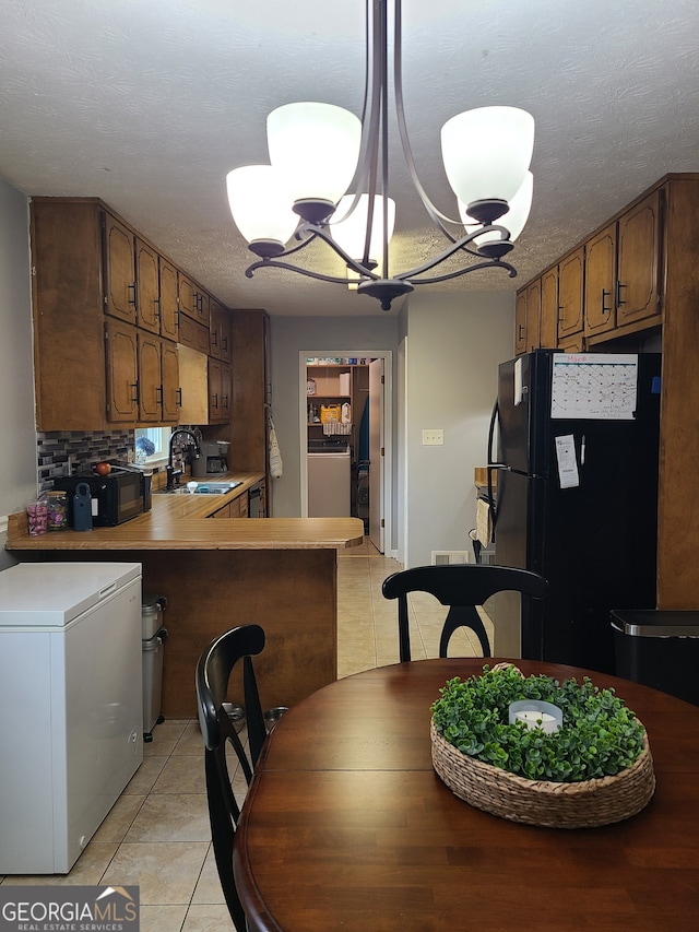 kitchen featuring white refrigerator, black refrigerator, kitchen peninsula, a chandelier, and sink