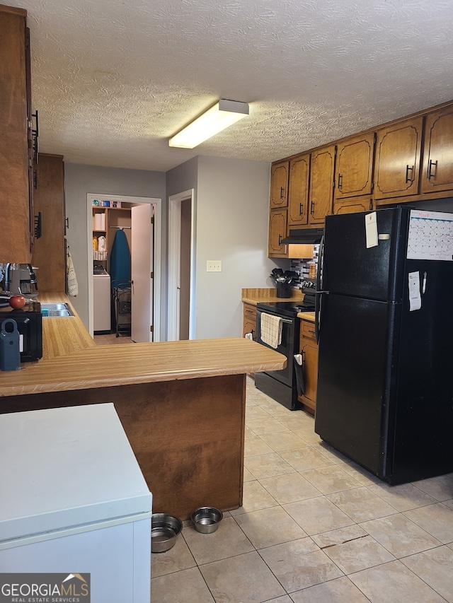 kitchen featuring black appliances, kitchen peninsula, a textured ceiling, and washer / dryer