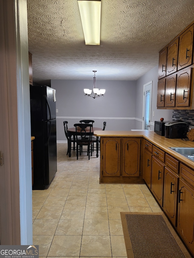 kitchen featuring kitchen peninsula, light tile patterned floors, an inviting chandelier, black refrigerator, and pendant lighting