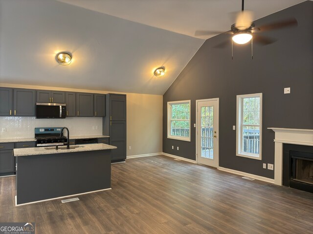 kitchen featuring black gas range, sink, a center island with sink, dark wood-type flooring, and light stone counters