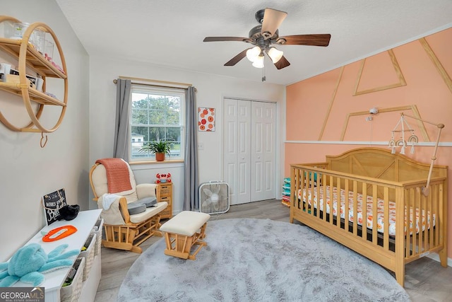 bedroom with a crib, wood finished floors, a ceiling fan, and a closet