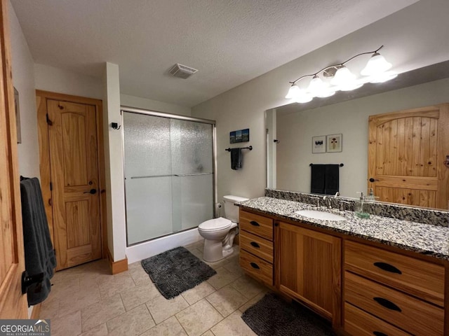 bathroom featuring tile patterned floors, toilet, a shower with door, a textured ceiling, and vanity