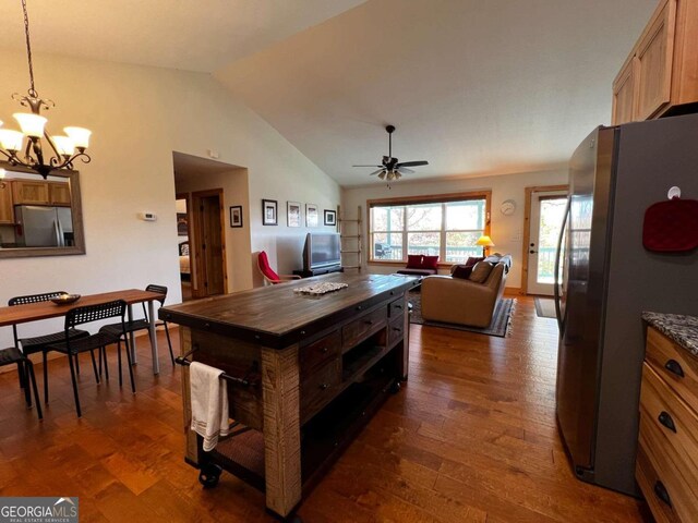 dining room with ceiling fan with notable chandelier, dark hardwood / wood-style floors, and vaulted ceiling