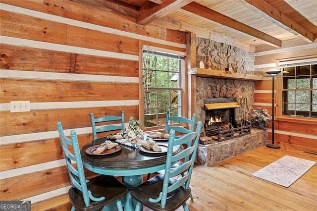 dining area with a stone fireplace, wood-type flooring, wood walls, wooden ceiling, and beamed ceiling