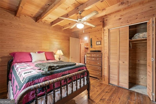 bedroom with a closet, wooden walls, hardwood / wood-style floors, beamed ceiling, and ceiling fan